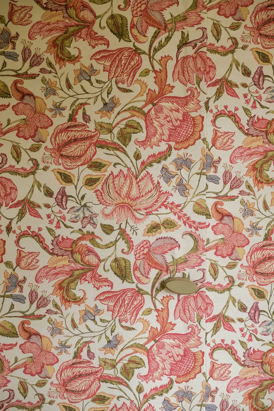 Pink and red floral wallpaper with green leaves covering a concealed cabinet door with a small handle