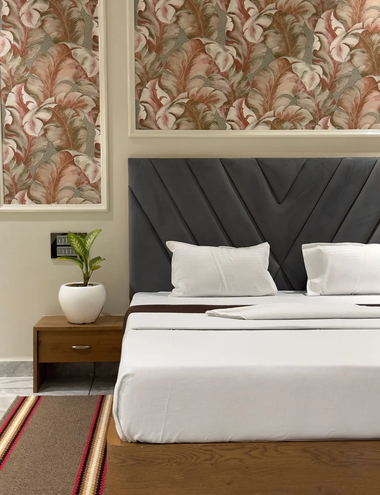 Large rust and cream leaf-patterned wallpaper above a charcoal headboard and wooden bedside table